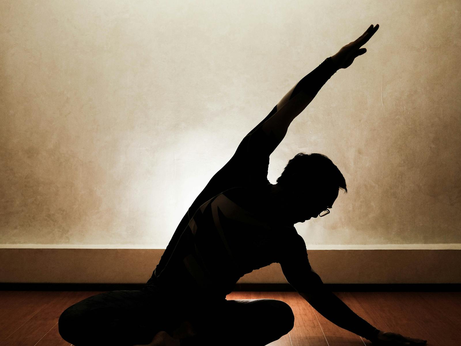 A vinyasa flow silhouette against a warm-lit wall — Open class